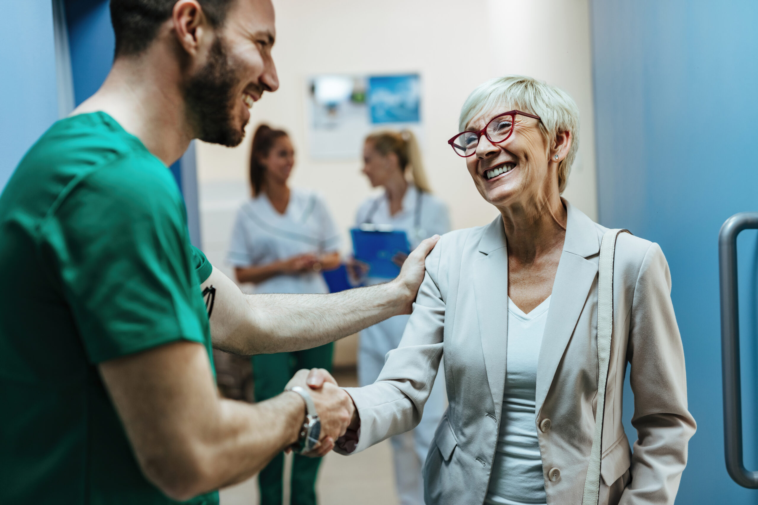 Happy senior woman shaking hands with a surgeon in a hospital ha