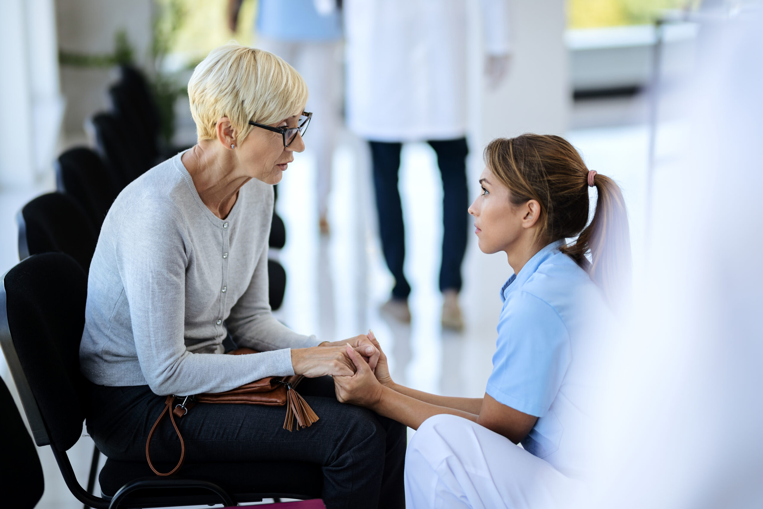 Caring nurse consoling mature woman in waiting room at medical c